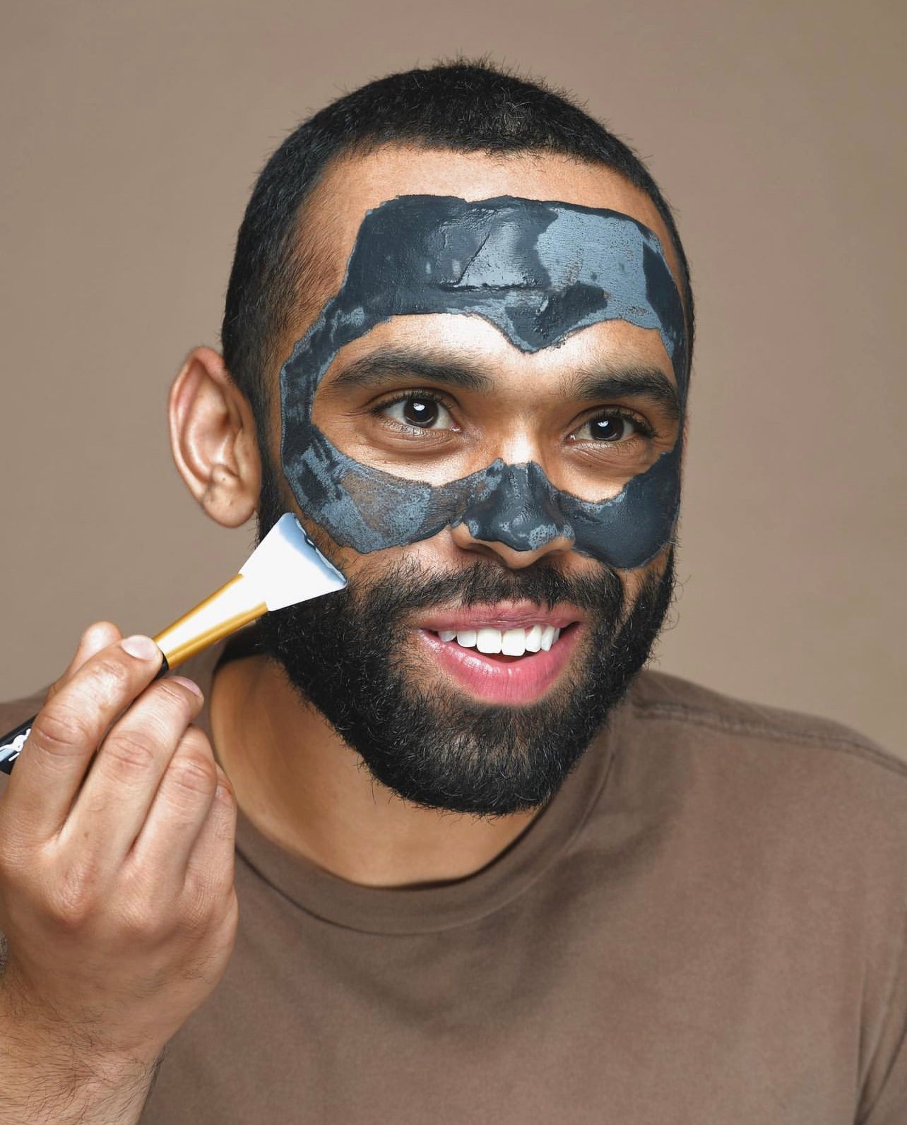 LATINO MAN PUTTING ON CHARCOAL LAVA SALT DRY MASK, A NATURAL FACIAL WITH A BROWN SHIRT